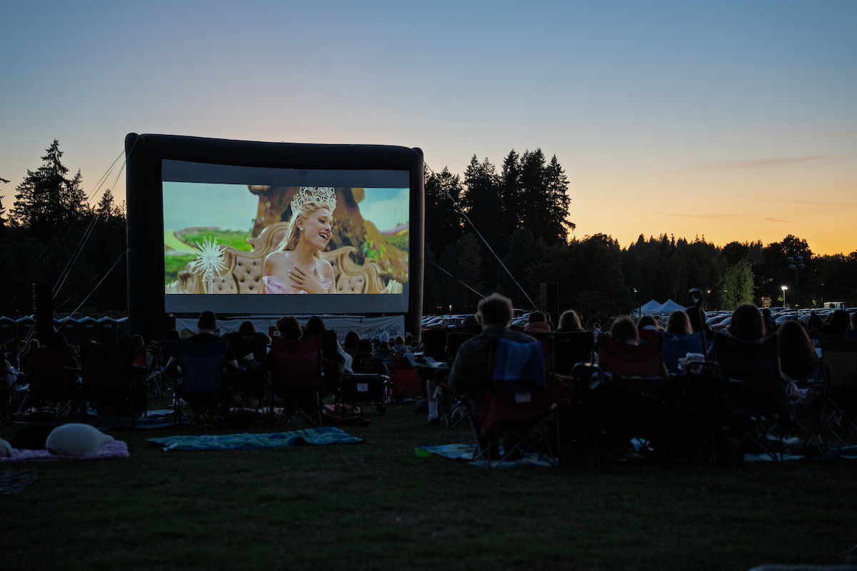People watch an outdoor movie with trees in the background