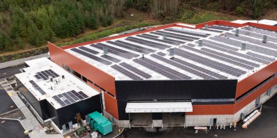 An aerial view of the South County Recycling and Transfer Station, with orange and black walls, and solar panels covering the roof.
