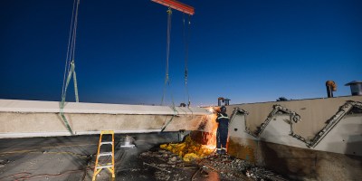 A welder works on a rooftop at sunset.