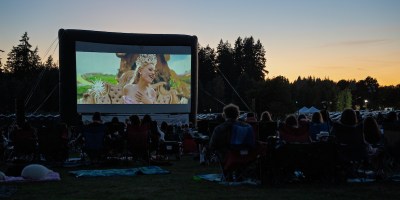 People watch an outdoor movie with trees in the background